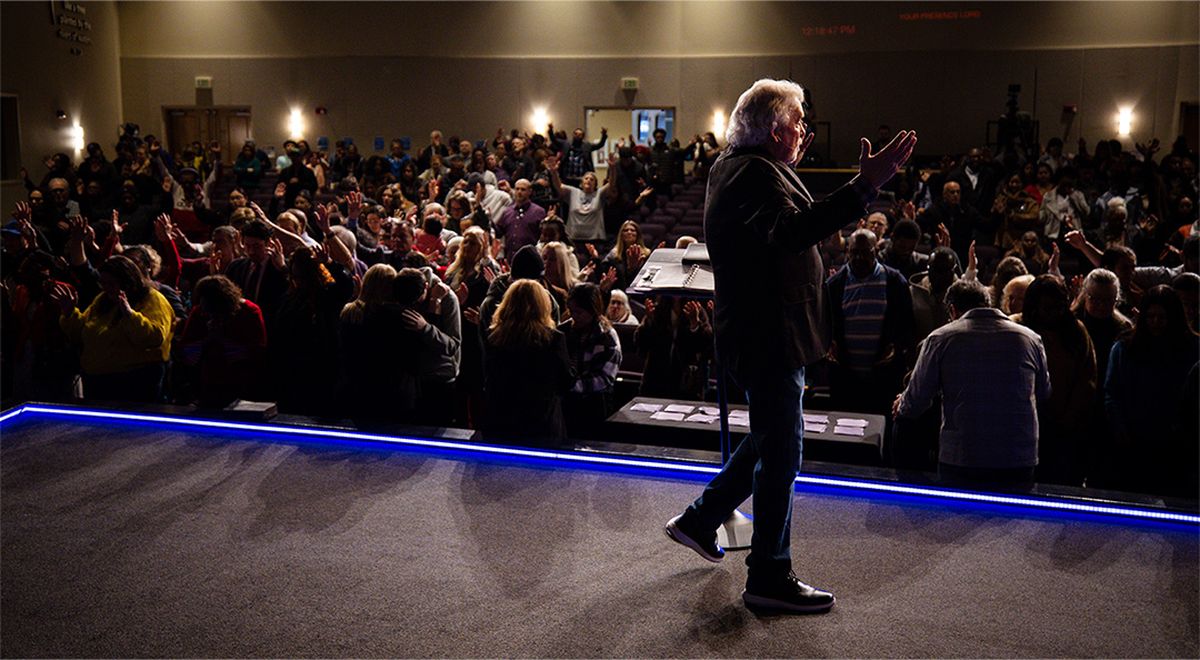 Pastor Jack preaching from the stage as the congregation lifts their hands