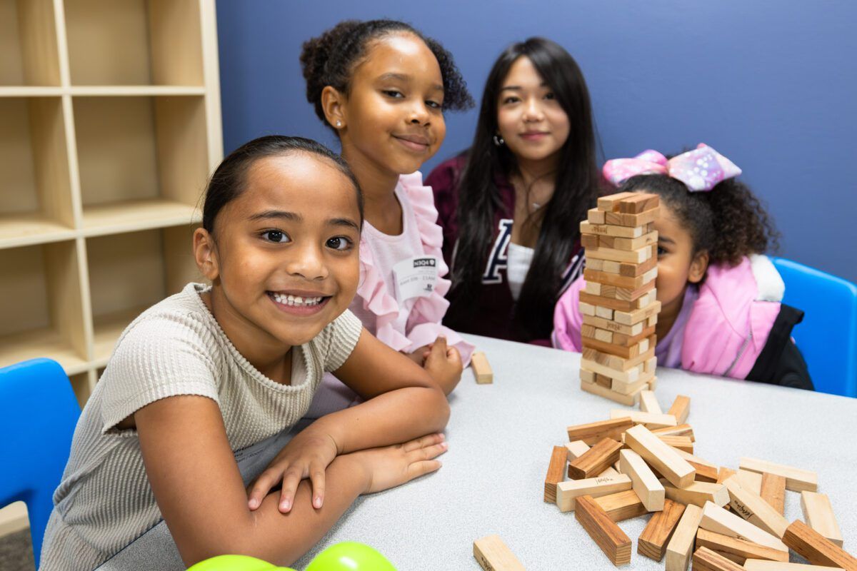 Smiling girls play a block-stacking game at a Kids Life table
