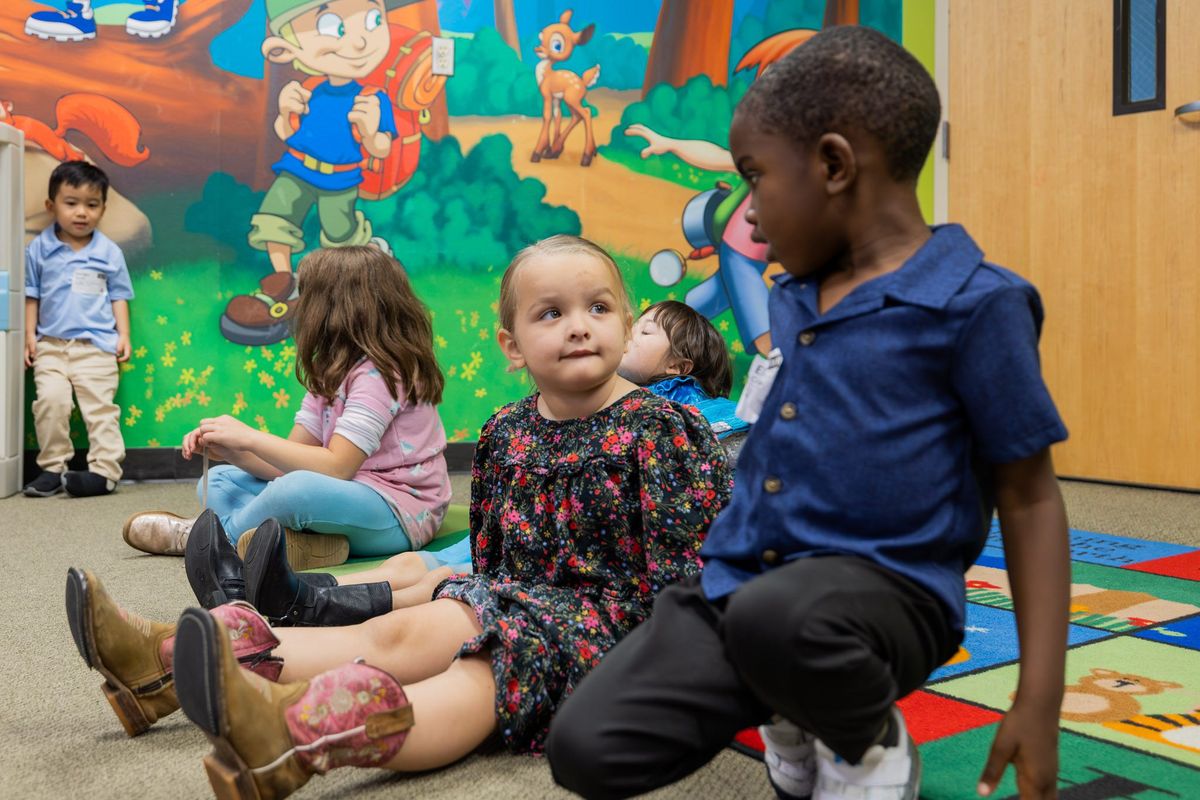 Young children sit together on a colorful rug in a Kids Life classroom