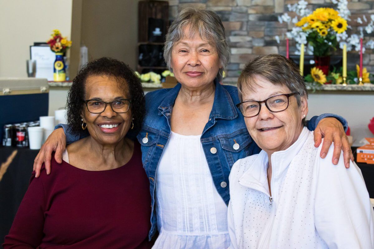 Three women from Legacy Seniors smile arm in arm